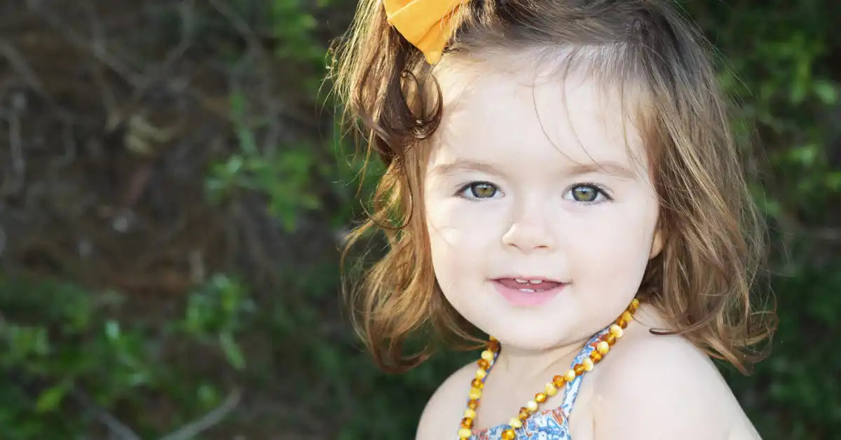 Smiling toddler with a yellow bow and amber necklace.